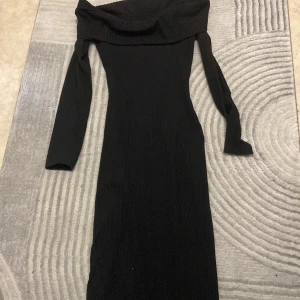 Svart ribbad långklänning offshoulder - Snygg svart långklänning med ribbad struktur och offshoulder-design. Klänningen har långa ärmar och en slits baktill som ger extra edge. Materialet är stickat och känns mjukt mot huden. Perfekt för dig som gillar stilrena och trendiga plagg.