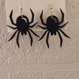  Helt nya halloween Svarta örhängen med spindelmotiv - Helt nya  svarta örhängen i form av spindlar, perfekta för dig som gillar statement-smycken. De är tillverkade i lätt syntetmaterial passar till halloween 