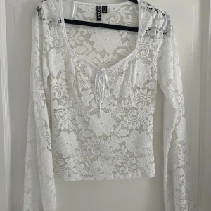 Vit spetsblus med snörning från Pieces - Vit långärmad blus i genombruten spets med blommigt mönster. Toppen har u-ringad hals med snörning framtill och är figurnära i passformen. Passar en storlek S också!