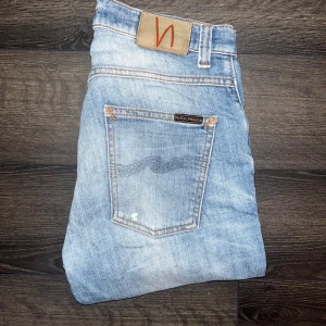 Nudie Jeans - Snygga ljusblå jeans från Nudie Jeans med femficksdesign och orangea sömmar. Jeansen har en fräsch tvättad look och är tillverkade i mjukt jeanstyg. Midja 38cm, längd 103cm. Ifall det inte finns någon bild i annonsen där jag bär plaggen jag säljer så är det för att jag ej kan ha storleken heller passformen, så kolla måtten för storlek och googla på modellnamnet för passform 😉OBS Se defekt på sista bilden. S2
