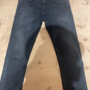 Replay Grover jeans i mörkblå denim - Säljer ett par Replay Grover jeans i mörkblå tvätt med klassisk femficksdesign. Jeansen har rak passform och normal midja, tillverkade i mjuk och slitstark bomullsdenim. Snygga detaljer med Replay-logga på fickan och metallknapp framtill. Midja 30 och längden är 34, jag är 186cm och de sitter perfekt. Inga defekter eller sådant!