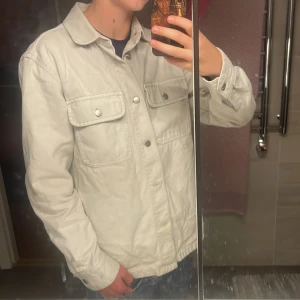 Vit overshirt från MNG Man, storlek M - Snygg vit overshirt från MNG Man med klassisk krage och två stora bröstfickor med knappar. Skjortan har en loose passform och är tillverkad i bomull. Perfekt att slänga över en t-shirt för en chill look.