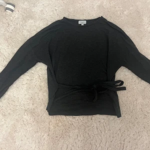 Svart/grå långärmad tröja med knyt från Bik Bok - Mysig svart långärmad tröja från Bik Bok, modell Balance. Tröjan har ett snyggt knytband i midjan som ger en cool och avslappnad look. 