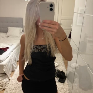 Svart tubtopp med paljettdetaljer - Säljer en svart tubtopp med snygga paljettdetaljer i silver framtill. Toppen har en dragkedja i ryggen och sitter tight. Perfekt för dig som vill sticka ut lite extra med en glittrig touch.