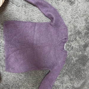 Lila stickad v-ringad tröja - Mysig lila stickad tröja med v-ringning och långa ärmar. Perfekt för lager-på-lager och chill dagar. Tröjan har en enkel design och är supermjuk, vilket gör den till ett måste i garderoben.