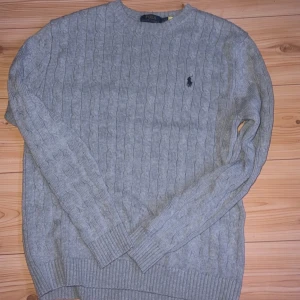 Grå kabelstickad tröja Polo Ralph Lauren - Säljer en grå kabelstickad tröja från Polo Ralph Lauren. Tröjan har rund halsringning, ribbade muddar och det klassiska broderade logotypen på bröstet. Perfekt för lager-på-lager och passar till jeans eller chinos. Skulle säga att passformen är mellan S/M