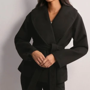 Svart omlott kappa med bälte - Snygg svart kappa med bred krage och omlott-design. Jackan har ett matchande bälte i midjan och långa ärmar. Helt oanvänd🥰 Funkar nästan till att kläder😍 har såklart egna bilder bara att säga till så skickar jag mer bilder. Ny med prislapp😍