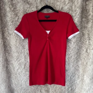 Röd ribbad topp från Canard Collection - Röd ribbad topp med v-ringning och två små knappar framtill. Står L på lappen men är snarare en S/M.