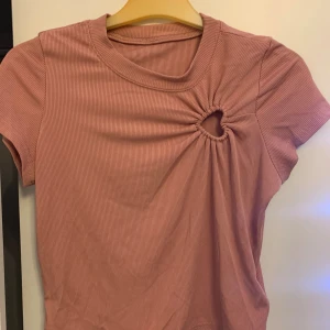 Rosa ribbad topp med cut-out från Dazy - Säljer en rosa ribbad topp från Dazy med cool cut-out detalj vid axeln. Toppen har rund hals, korta ärmar och är gjord i mjukt stretchigt material. Perfekt för dig som gillar trendiga detaljer och vill sticka ut lite extra. Det är Xs men går att använda som S också 