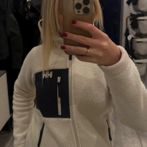 Vit teddyjacka från Helly Hansen - Säljer min vita teddyjacka från Helly Hansen då den är för liten för mig. Teddyjackan är nästan helt nyskick och knappt använd💕köparen står för frakt!