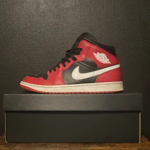 Nike Air Jordan 1  mids - Säljer ett par klassiska Nike Air Jordan 1 Highs i färgen Bred. Skorna har svart och rött skinn med vita swooshes och svarta skosnören. Ikonisk Air Jordan-logga på sidan och röd yttersula. Perfekta för dig som vill sticka ut med en tidlös sneaker.