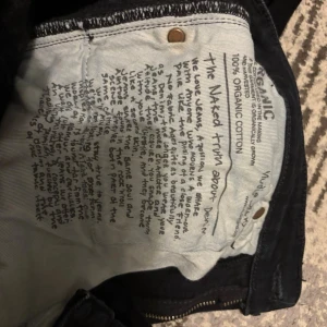 Svarta Nudie Jeans, storlek W28 L32 - Säljer ett par svarta jeans från Nudie Jeans i modellen med klassisk femficksdesign och snygga detaljer på bakfickan. Jeansen är tillverkade av 100% ekologisk bomull och har en rak passform. Perfekt för dig som gillar stilrena och hållbara jeans. Gylfen är lite trasig men går och laga enkelt, pris kan diskuteras. 