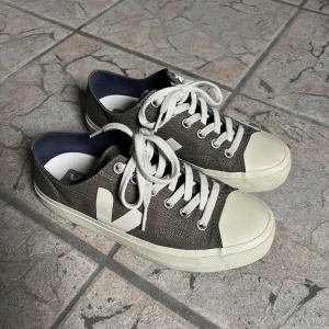 Kakhi gröna Veja sneakers med vit sula - Snygga sneakers från Veja i grön textil med vit gummisula och vit logga på sidan. Skorna har rund tå, snörning med vita bomullssnören och metallöglor. Insidan är mörkblå och yttersulan har ett hexagonmönster. Perfekt för dig som gillar stilrena och klassiska sneakers. Knappt använda då de ej passar mig. Väldigt bra skick, förutom små märken längst fram (se bild 3.)