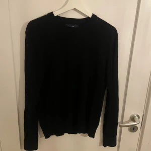 Svart stickad tröja från Riley - En stilren svart stickad tröja från Riley i storlek L men passar snarare M. Tröjan har rund halsringning och långa ärmar, perfekt för lager-på-lager under kyligare dagar. Enkel och klassisk design som funkar till allt.