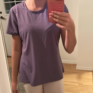 Lila tränings T-shirt - En stilren lila tränings T-shirt med rundad hals. Ganska lös i passformen och passar perfekt för dig som gillar en avslappnad tränings look. Endast använd en gång.