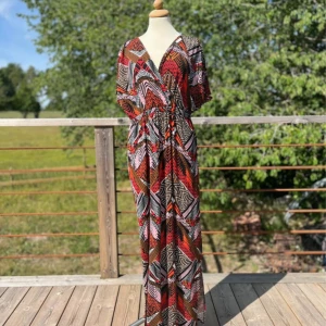 Mönstrad långklänning från Fransa - Säljer en färgstark långklänning från Fransa med coolt grafiskt mönster i rött, svart, vitt och brunt. Klänningen har v-ringning, korta ärmar och resår i midjan för en snygg passform. 