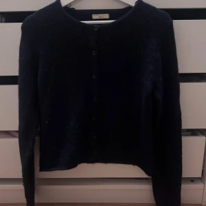 Mörkblå kofta Gina Tricot Premium Quality - Säljer en mörkblå, fluffig kofta från Gina Tricot. Koftan har rund halsringning, långa ärmar och knäppning framtill med svarta knappar. Perfekt för lager-på-lager och riktigt mysig till höst och vinter.