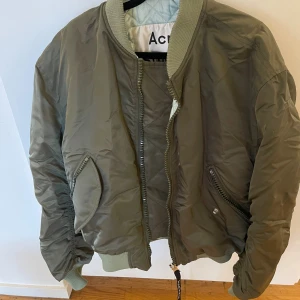 Olivgrön bomberjacka från Acne Studios - Olivgrön bomberjacka från Acne Studios. Jackan har en klassisk bomberjacka-design med ribbade muddar och krage. Den har en dragkedja fram och fickor på sidorna. Jackan är i riktigt fint skick. Rökfritt hem. Skickar paket som spårbart.
