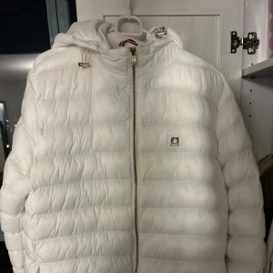 Vit pufferjacka från Beverly Hills Polo Club - L/XL - Snygg vit pufferjacka från Beverly Hills Polo Club med huva och dragkedja framtill. Jackan har quiltad design, guldiga detaljer vid snörningen och logga på bröstet. Perfekt för kalla dagar och ger en clean, fräsch look. Har bara använt den 2 gånger, finns inga alls skador eller smuts eller nåt annat på den. Den passar storlek L och XL, L om du vill ha en lite stor jacka och XL passar den nog perfekt, finns chans att den passar XXL. Priset kan diskuteras💕