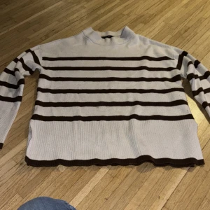 Randig beige tröja från Vero Moda - Säljer en beige stickad tröja från Vero Moda med bruna horisontella ränder. Tröjan har lång ärm, ribbade muddar och en klassisk rund hals. Perfekt för dig som gillar en chill och stilren look.