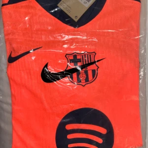 Barça orange matchtröja Nike XL - Säljer en Barcelona fotbollströja i stark orange med mörkblå detaljer, Nike-logga och Spotify sponsortryck. Tröjan har klubbmärket på bröstet och är tillverkad i lätt, ventilerande polyester. Perfekt för dig som vill sticka ut på planen eller visa support för Barça.