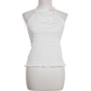 Vit topp från Nelly - Säljer en vit halterneck topp från Nelly i storlek XS. Toppen är ärmlös med knyt i nacken och ryggen, har en lätt rynkad struktur och är tillverkad i mjuk polyesterblandning. Perfekt för en fräsch och trendig look i sommar.