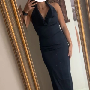 Marinblå långklänning med halterneck - Snygg marinblå långklänning med halterneck och draperad urringning. Klänningen har en figurnära passform som framhäver siluetten och är ärmlös med öppen rygg. Perfekt för dig som vill ha en elegant och stilren look. Endast använd en gång till fest så ren och ny!