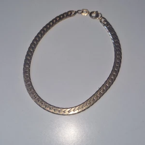 Guldigt kedjearmband med lås - Snyggt armband i guldton med platt, flätad kedja och klassiskt ringlås. Perfekt för dig som gillar stilrena och tidlösa smycken med lite extra glans. Passar till alla outfits och är lätt att matcha med andra accessoarer.