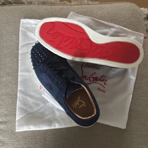 Christian Louboutin mörkblå sneakers - Säljer ett par mörkblå sneakers från Christian Louboutin med ikonisk röd sula och spetsiga nitar framtill.  Storlek 44 köpte för 2500 men passade inte så säljer de helt nya
