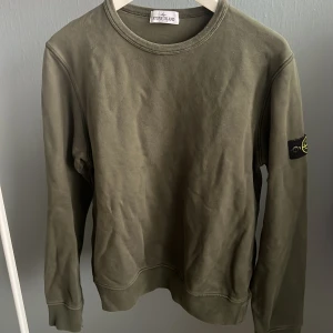 Olivgrön Stone Island sweatshirt - Säljer en olivgrön sweatshirt från Stone Island Junior med klassisk rund hals och ikonisk patch på ärmen. Tröjan är i mjuk bomull och har ribbade muddar vid ärmslut och nederkant. Perfekt för dig som gillar streetwear och vill ha en clean look.