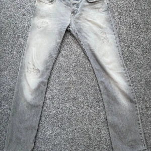 Gråa jeans - Snygga grå jeans med slitna och lagade detaljer på benen. Jeansen har klassisk femficksdesign och raka ben. Färgen är ljusgrå med en tvättad look som ger en cool vibe. Perfekta för dig som gillar en avslappnad och trendig stil.