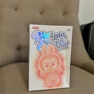 Labubu Pop Mart Big Into Energy Blind Box - Pop Mart Big Into Energy blind box med vinyl plush pendant. Förpackningen är oöppnad och i gott skick, med endast mindre veck på sidan. Perfekt för samlare eller som present till fans av Pop Mart-figurer.