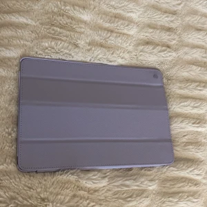 Holdit iPad fodral lila - Snyggt lila iPad-fodral från Holdit. Passar perfekt för att skydda din iPad mot repor och stötar. Fodralet har stativfunktion och magnetisk stängning. Mycket fint skick, inga synliga defekter eller slitage. Perfekt för dig som vill ge din iPad ett stilrent skydd. Inte använt pga förstort.