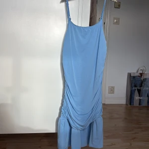 Ljusblå omlottklänning från SHEIN - Supersöt ljusblå klänning från SHEIN med smala axelband och snygg drapering längs sidorna. Klänningen har volang nertill och är tillverkad i ett mjukt, stretchigt material. Perfekt för dig som gillar en feminin och trendig look.