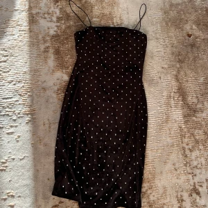 Svart klänning med pärlor - Supersnygg svart klänning med tunna axelband och täckt av små pärlor. Kort modell med figurnära passform och rak halsringning. Perfekt för dig som vill sticka ut med en glittrig och elegant look. Perfekt för fest/event!