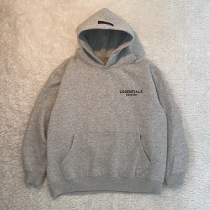 Grå Essentials Fear of God hoodie S - Säljer en grå hoodie från Essentials Fear of God i storlek S. Tröjan är helt ny men saknar prislapp, påsen finns med men är inte med på bild 👍. Tröjan är i 100% bomull, har huva, känguruficka och svart logga tryckt både fram och bak. Perfekt för en chill och stilren look. Tröjan sitter lite bagy men armarna sitter fint. Om du har några frågor är det bara att fråga 👍😊
