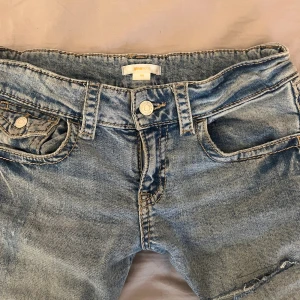 Ljusblå bootcut jeans från Gina Tricot - Snygga ljusblå jeans från Gina Tricot med bootcut passform och slitna detaljer på benen. Klassisk femficksmodell med knapp och dragkedja framtill. Jeansen har en cool tvätt och är gjorda i jeansmaterial med kontrastsömmar.