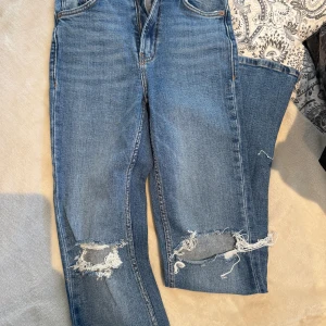 Blå ripped jeans från Zara, strl 34 - Snygga blå jeans från Zara i storlek 34 med slitna detaljer och hål vid knäna. Dom är bootcut och har en slits nertil