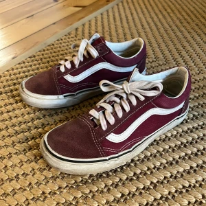 Vinröda Vans Old Skool sneakers - Säljer ett par klassiska Vans Old School sneakers i vinrött med vita detaljer och snörning. Skorna är slitna, men har en eller ett par somrar kvar. 