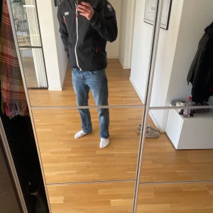 Vindjacka från Helly Hansen - Säljer en mörkblå tjock jacka  från Helly Hansen med vit dragkedja. Jackan har långa ärmar och en hög krage för extra skydd mot väder och vind.  Storleken är L och är i mycket bra skick! Perfekt för att håla sig varm i vinter. Tveka inte att höra av dig vid frågor