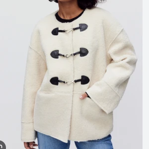Vit/beige teddyjacka  - Säljer en oversized vit teddyjacka från dobber med svarta detaljer och tre metallspännen framtill. Jackan har stora fickor, rund halsringning och är tillverkad i mjukt teddy-material. Perfekt för  höst- eller vinter. 