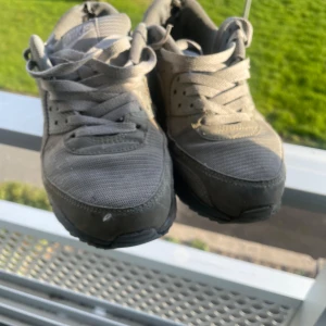 Nike Air Max 90 grå sneakers - Säljer ett par grå Nike Air Max 90 sneakers med klassisk siluett och synlig Air-dämpning i sulan. Skorna har snörning, rund tå och är tillverkade i en mix av syntet och textil. Perfekta för dig som gillar streetstyle och vill ha en ikonisk sneaker i garderoben.