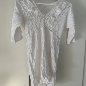 Vit klänning/morgonblus med spetsdetaljer - Vit klänning/blus med v-ringning och halvärmar. Klänningen har broderade spetsdetaljer och en slits på båda sidor. Uppskattas till storlek xs\s! Så fin på en sommarmorgon!