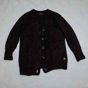 Svart kofta från Marc O'Polo XS - Mysig svart kofta från Marc O'Polo i storlek XS. Koftan är stickad med grov struktur, har knappar framtill och en liten metallbricka nertill. Materialmix av ull, mohair, viskos och polyamid gör den både varm och mjuk. Perfekt för lager-på-lager under kyliga dagar.