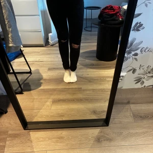 Svarta jeans med hål i knäna - Svarta jeans från lager 157 med hög midja och snygga slitningar på båda knäna. Klassisk femficksmodell med silverfärgade nitar och knapp. Jeansen har en rak passform och är tillverkade i ett stretchigt bomullsmaterial för extra komfort. Har alltid haft jeansen uppvikta så dom är inte slitna nertill, storlek XS. 