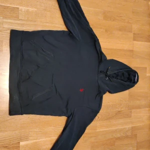 Svart hoodie från U.S. Polo Assn M - Svart hoodie från U.S. Polo Assn. i storlek M. Klassisk modell med huva och snörning, känguruficka framtill och röd broderad logga på bröstet. Perfekt för chill dagar och enkel att matcha med jeans eller joggers.