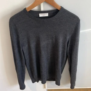 Mörkgrå stickad tröja Tiger of Sweden - Mörkgrå stickad tröja från Tiger of Sweden i klassisk modell med rund halsringning och ribbade muddar. Perfekt för lager-på-lager och enkel att matcha med jeans eller chinos. Materialet är mjukt och ger en clean look. Inga defekter. Pris kan diskuteras. 