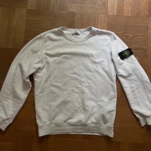 Vit sweatshirt från Stone Island - Vit sweatshirt från Stone Island med klassisk rund hals och ikonisk logga på vänster ärm. Tröjan har en clean look med ribbade muddar och är tillverkad i mjuk bomull. Liten färg defekt på axeln. Storlek M passar även S. Kom gärna med prisförslag till denna!✌️