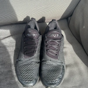 Svarta Nike Air 270 sneakers - Säljer ett par svarta Nike Air 270 sneakers med ventilerande mesh-ovandel och klassisk snörning. Skorna har en chunky sula och diskreta loggor på tungan och sidan. Perfekta för dig som gillar sportig och stilren look. Lite söndriga på högra skon men inget som man märker av när man har på sig de.