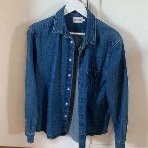 Blå jeansskjorta från East West - Klassisk blå jeansskjorta från East West i 100% bomull. Skjortan har lång ärm, bröstficka och knappar framtill. Perfekt oversized fit för en avslappnad look.